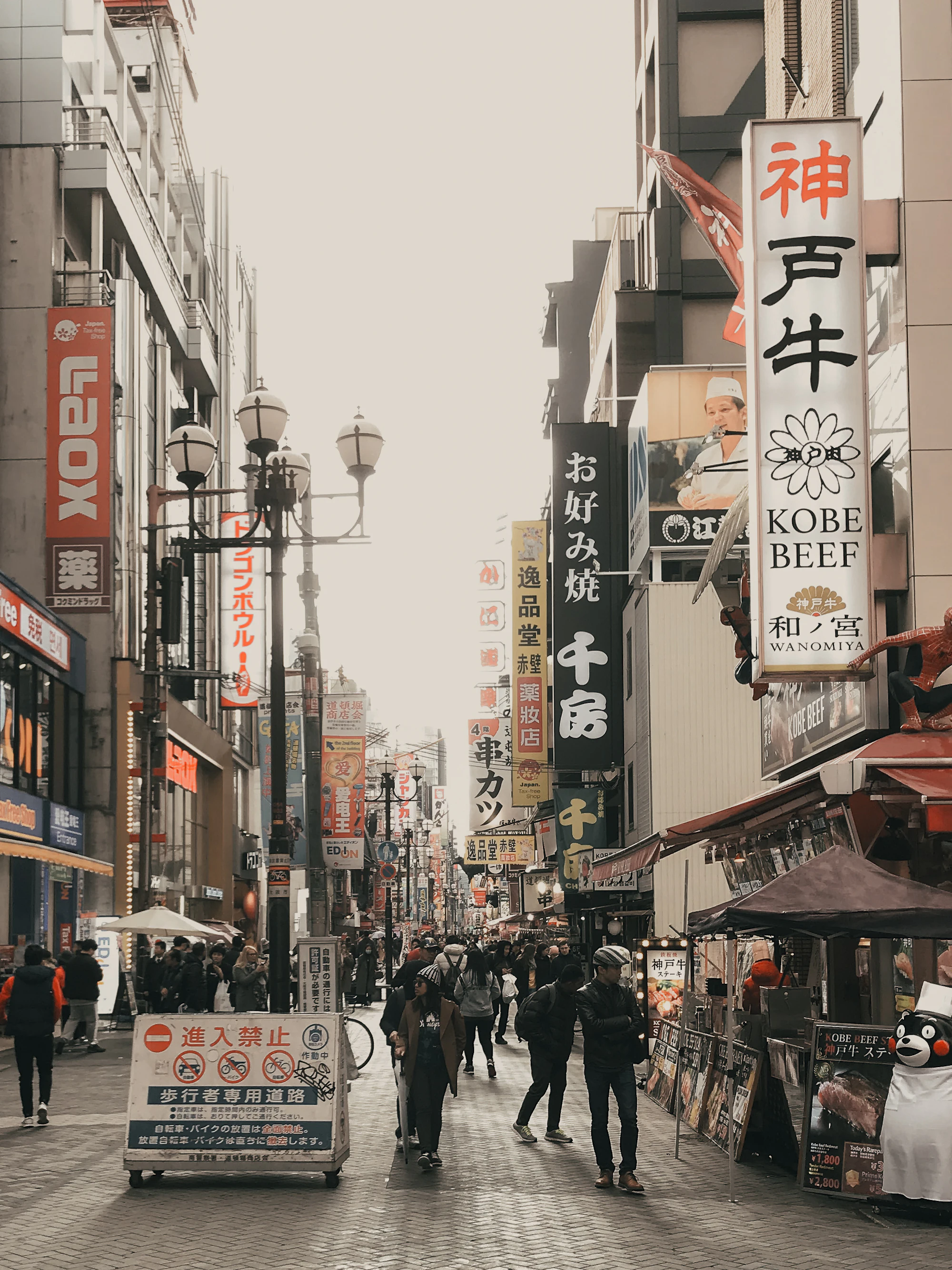 A busy shopping street in Osaka under a pale sky, hung with Japanese signs on both sides